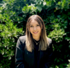 A person smiling in front of a bush.