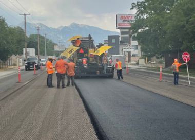A group of men in orange vests standing on the side of a road.